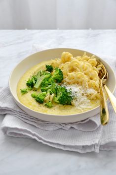 a white bowl filled with pasta and broccoli on top of a napkin next to a fork