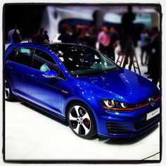 a blue volkswagen car is on display at an auto show with people in the background