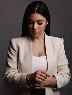 a woman in a white jacket and black skirt with her hands folded over her chest