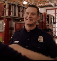 a man in uniform standing next to a firetruck and talking to someone else