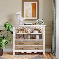 a white cabinet sitting in front of a potted plant