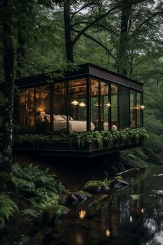 a small cabin in the middle of a forest next to a river with lights on