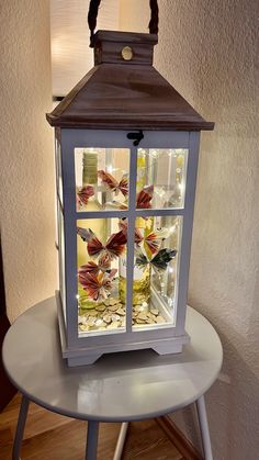 a lighted lantern sitting on top of a white table next to a lamp with butterflies in it