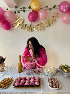 a woman sitting at a table in front of a pink cake and cupcakes