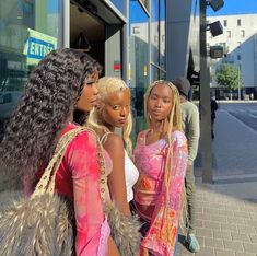 three beautiful young women standing next to each other on a city street in front of a building