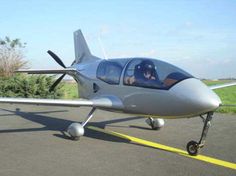 a small silver airplane sitting on top of an airport tarmac next to a field