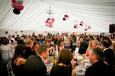 a large group of people sitting at tables in a room with white and pink decorations