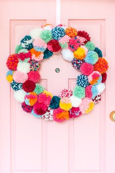 a pink door with a colorful pom - pom wreath hanging on it's side