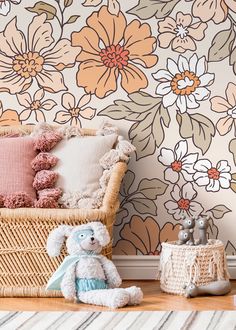 a teddy bear sitting on the floor next to a basket with pillows and stuffed animals