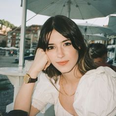 a woman sitting at an outdoor table with her hand on her chin and looking off to the side