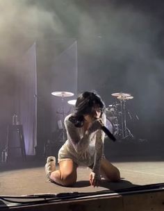 a woman kneeling down on the ground with a microphone in her hand and lights behind her