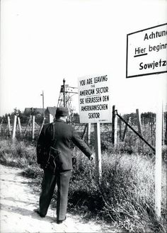 a man walking down a dirt road next to a sign