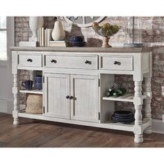 a white wooden buffet table with drawers and plates on the top, in front of a brick wall