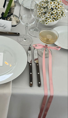 the table is set with white plates, silverware and pink ribbon on it's edge