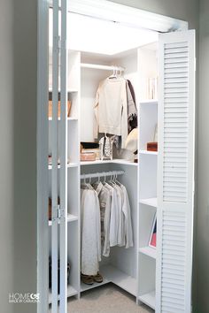 an open closet with clothes and other items on shelves in the corner, all white