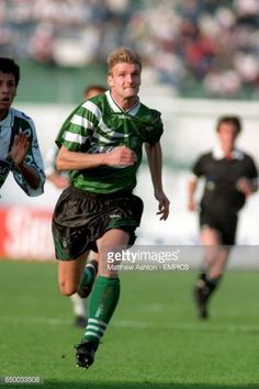 two soccer players running after the ball during a game in green and white striped shirts