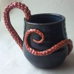 an octopus mug is sitting on the table next to a cup with its tentacles wrapped around it