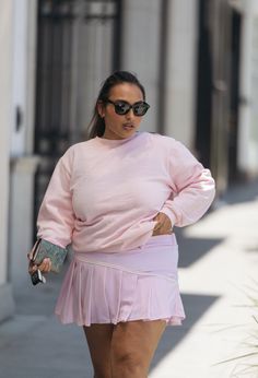 a woman walking down the street in a pink dress and black sunglasses with her hand on her hip