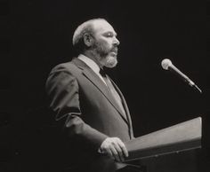 a black and white photo of a man speaking at a podium with a microphone in front of him