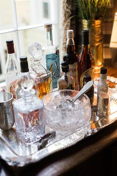 an assortment of liquor bottles and glasses sitting on a tray next to a window sill