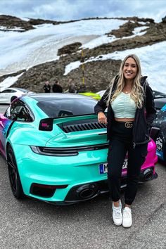 a woman standing next to two sports cars