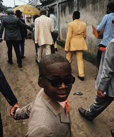 a young boy wearing sunglasses and standing in the middle of a street with other people