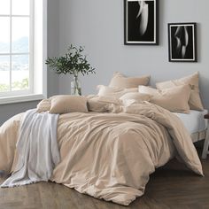 a bed with grey sheets and pillows in a room next to a window, framed pictures on the wall