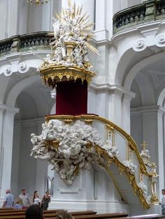 an ornate staircase in a church with gold and white decorations on the top, along with people standing around