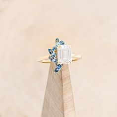 a ring with an emerald and blue topazte surrounded by small diamonds on a wooden stand