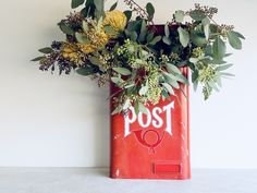 a red post box with greenery in it and the word post painted on it