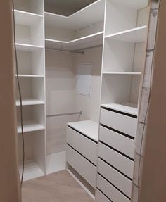 an empty walk in closet with white shelving and drawers on each side, along with no doors