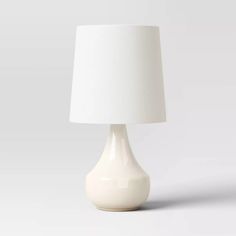 a white table lamp with a white shade on the base and a light bulb at the end