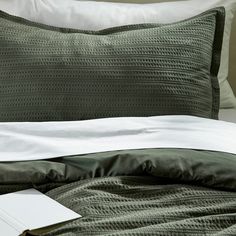 a close up of a bed with green and white sheets, pillows and an open book