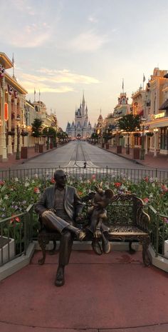 a statue sitting on top of a bench in front of a street filled with flowers