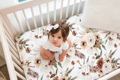 a baby sitting in a white crib with flowers on it's bed sheet