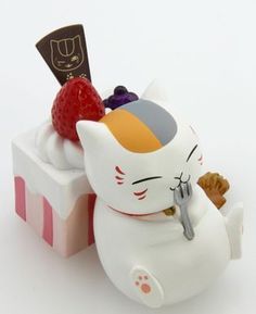 a cat figurine sitting on top of a box filled with berries and strawberries