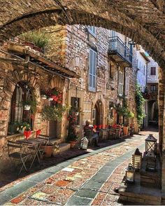 an alley way with tables and chairs on the side, surrounded by stone buildings that are lined with potted plants