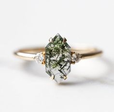 a close up of a ring on a white surface with green and white flowers in it