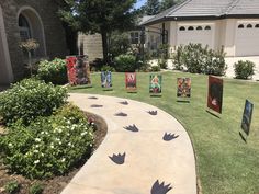 several pieces of artwork on display in front of a house with flowers and bushes around it