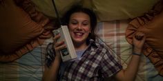 a woman laying in bed with an old style video game controller on her chest and smiling at the camera