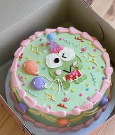 a green cake with pink icing in a box on top of a wooden table