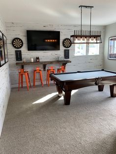 a pool table sitting in the middle of a living room next to orange chairs and a flat screen tv