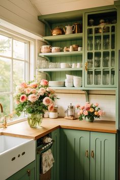 a kitchen with green cabinets and pink flowers in the vases on the window sill