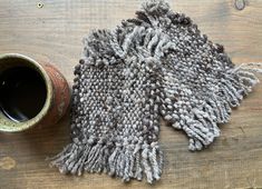 a gray and white knitted scarf next to a brown vase on a wooden table