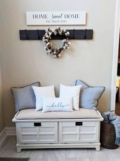 a white bench with some pillows on it and a wreath hanging above the bench is a sign that says home sweet home