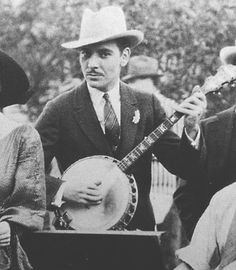 an old black and white photo of a man holding a banjo guitar in front of other people
