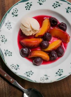 a white plate topped with fruit and ice cream on top of a wooden table next to a spoon