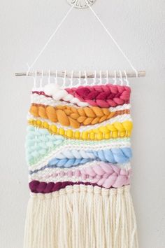 a multicolored wall hanging on a white wall next to a wooden rack with yarn