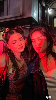 two young women standing next to each other in front of a building with red light