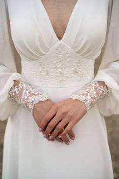 a woman in a white dress holding her hands on her chest and wearing an elegant lace cuff